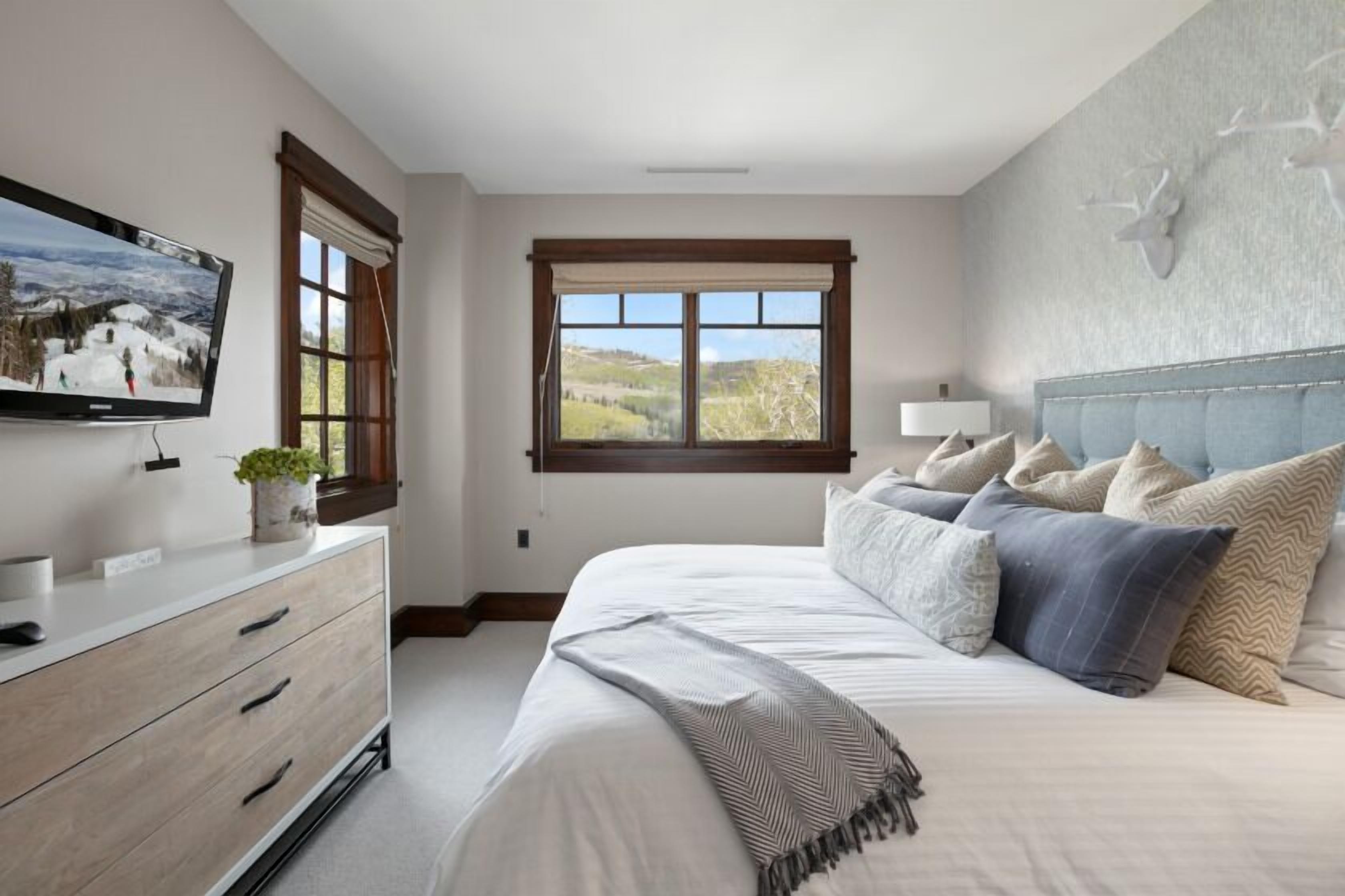 A bedroom with a bed, a dresser, a television, and a window with a view of a landscape.