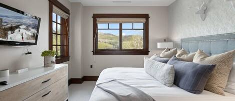A bedroom with a bed, a dresser, a television, and a window with a view of a landscape.