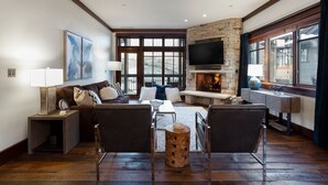 A cozy living room with a stone fireplace, comfortable seating, and large windows offering a view of the outdoors. - Arrowleaf Lodge - Two Bedroom Condo Residence #209 by Deer Valley Resort (Park City)