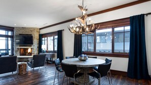 A spacious room with a stone fireplace, a round dining table with chairs, and a large window with curtains. - Arrowleaf Lodge - Two Bedroom Condo Residence #209 by Deer Valley Resort (Park City)