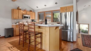 A modern kitchen with wooden cabinets, a stainless steel refrigerator, and a bar area with stools.