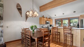 A spacious kitchen with wooden cabinets, a central island with bar stools, a dining table with chairs, and a chandelier.
