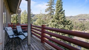 A wooden deck with two lounge chairs and a red railing overlooking a forested valley.