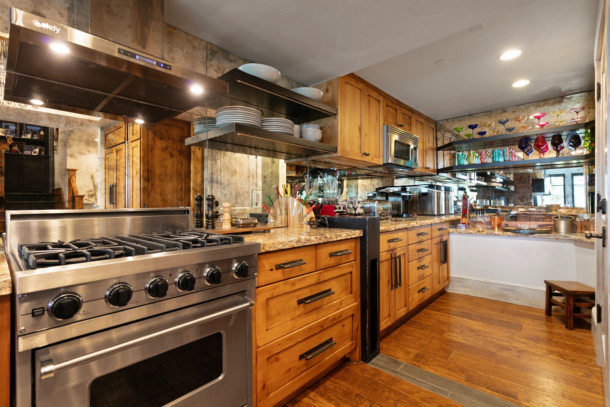 Una cocina moderna con electrodomésticos de acero inoxidable, armarios de madera y una variedad de cristalería exhibida en estantes.
