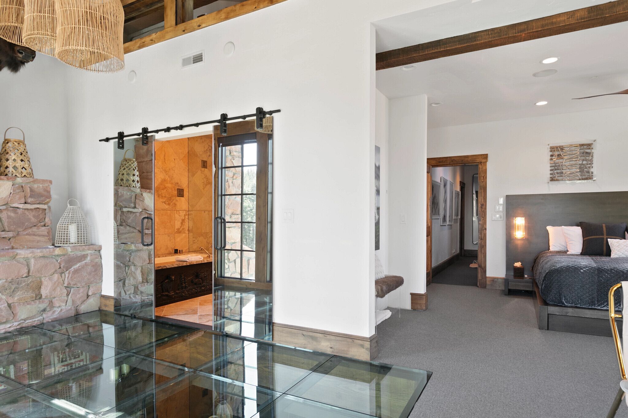 A spacious room with a glass table, a bed with a headboard, and a stone wall.