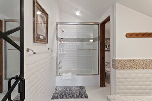 Ein modernes Badezimmer mit einer gläsernen Dusche, weißen Fliesenwänden und einer Holztür.