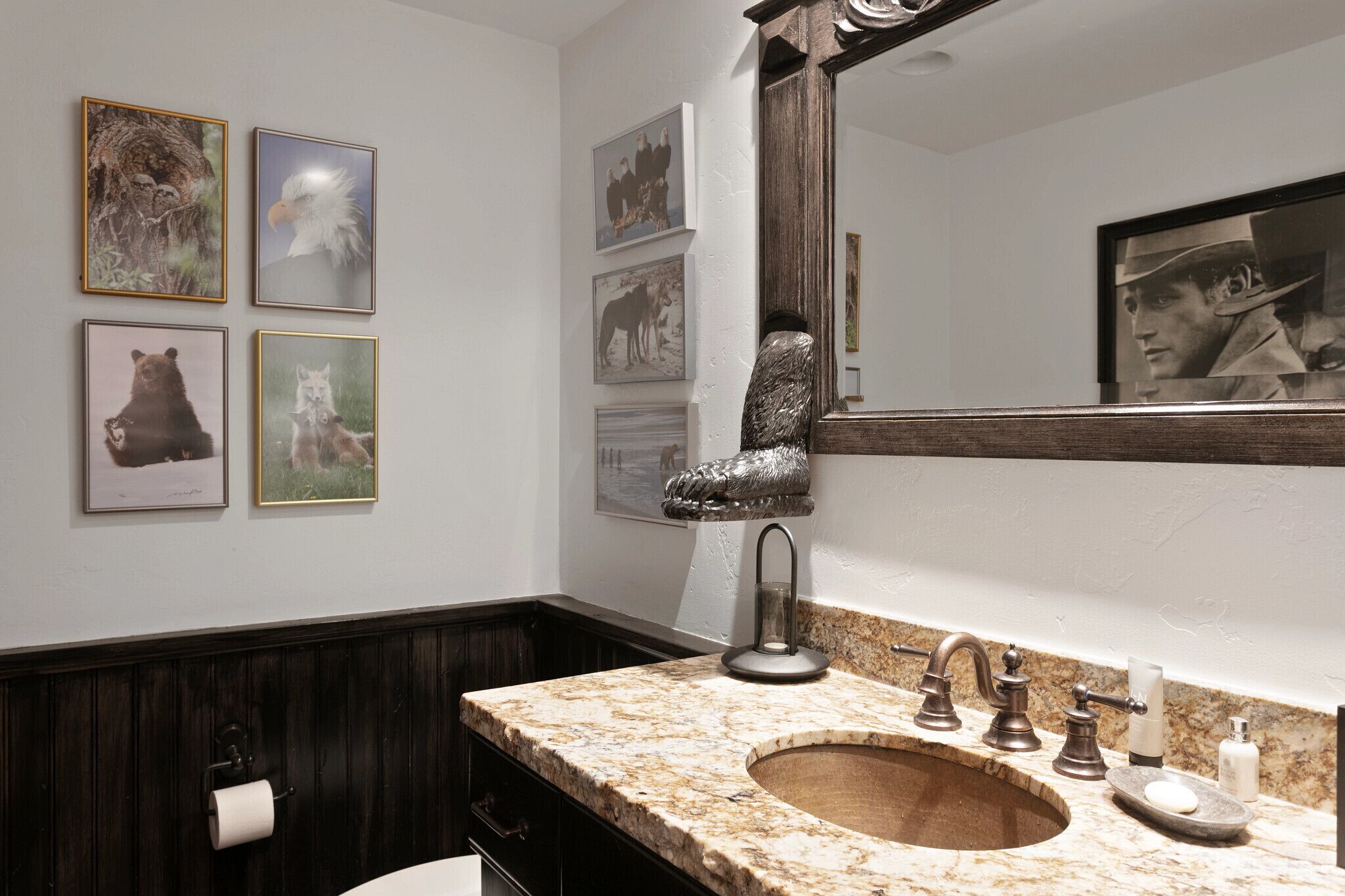 Une salle de bain avec un lavabo en marbre, des lambris en bois foncé et des photographies d’animaux sauvages encadrées accrochées au mur.