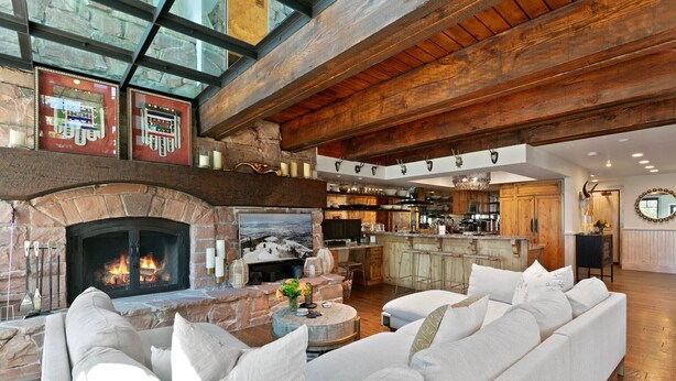A spacious living area with a stone fireplace, wooden beams, and a modern kitchen in the background. - Stag Lodge At Deer Valley Resort - 4 Bed W/ Spa #7 4 Bedroom Condo (Park City)