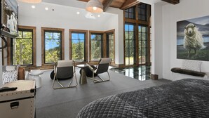 A spacious bedroom with large windows, a bed, a seating area with chairs, and a painting of a sheep. - Stag Lodge At Deer Valley Resort - 4 Bed W/ Spa #7 4 Bedroom Condo (Park City)