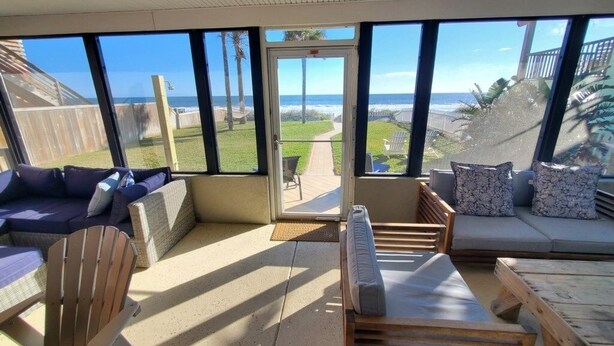 Une terrasse ensoleillée avec vue sur l’océan, aménagée avec un canapé, des fauteuils et une table en bois.