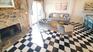 Un salon avec une cheminée en pierre, un sol à carreaux, un canapé gris et des fauteuils bleus.