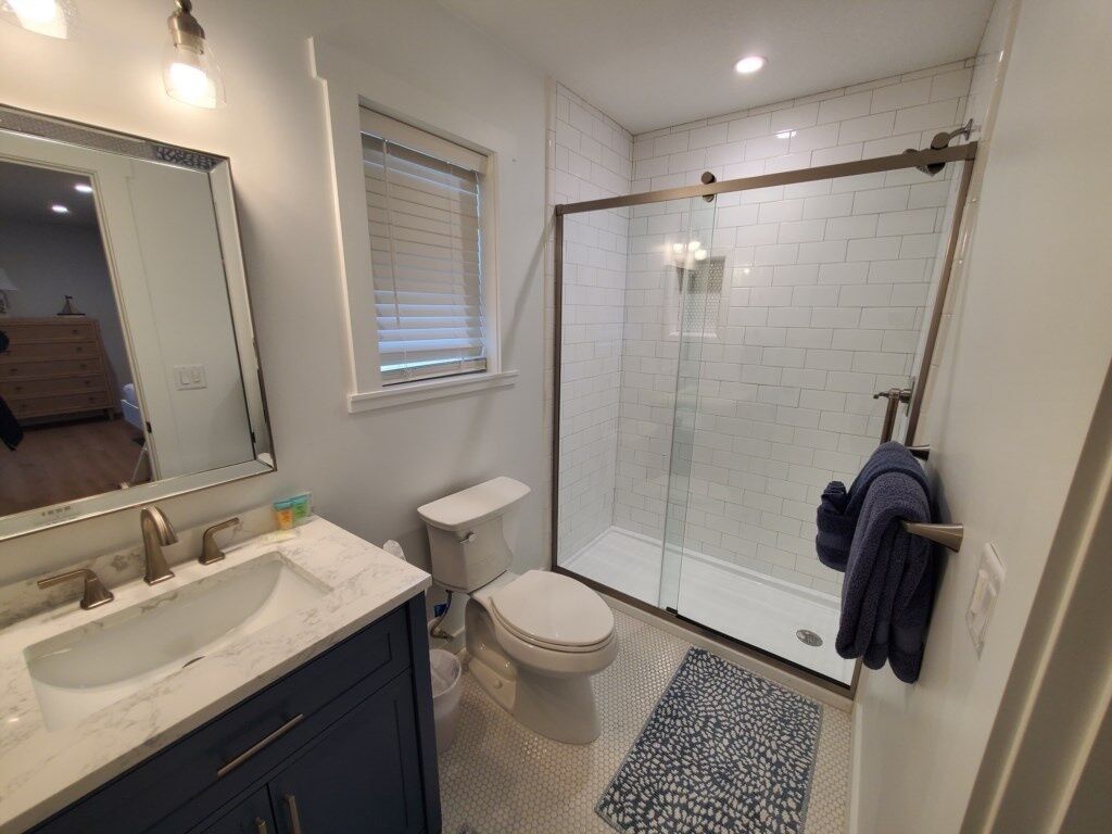 A bathroom with a glass-enclosed shower, a sink with a marble countertop, a toilet, and a large mirror.