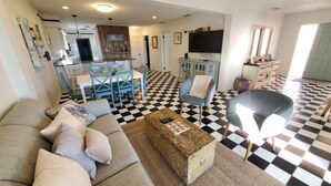 Un salon avec un sol à carreaux, un canapé, une table basse et un coin repas comprenant des chaises et une table.