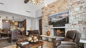 Un salón amplio con chimenea de piedra, muebles de cuero y un televisor montado en la pared.