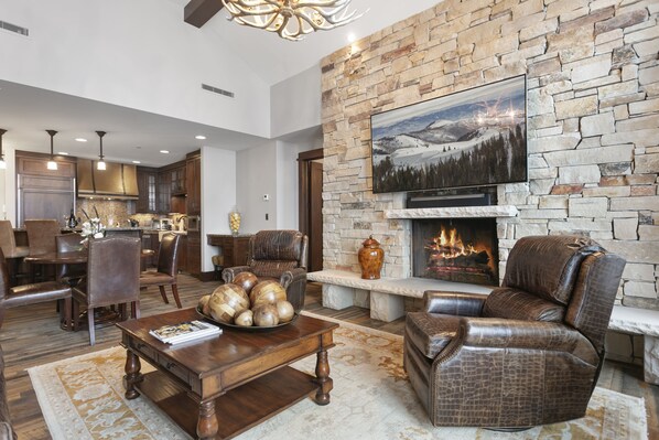 A spacious living room with a stone fireplace, leather furniture, and a television mounted on the wall. - Arrowleaf Lodge - Two Bedroom Condo #401 by Deer Valley Resort (Park City)