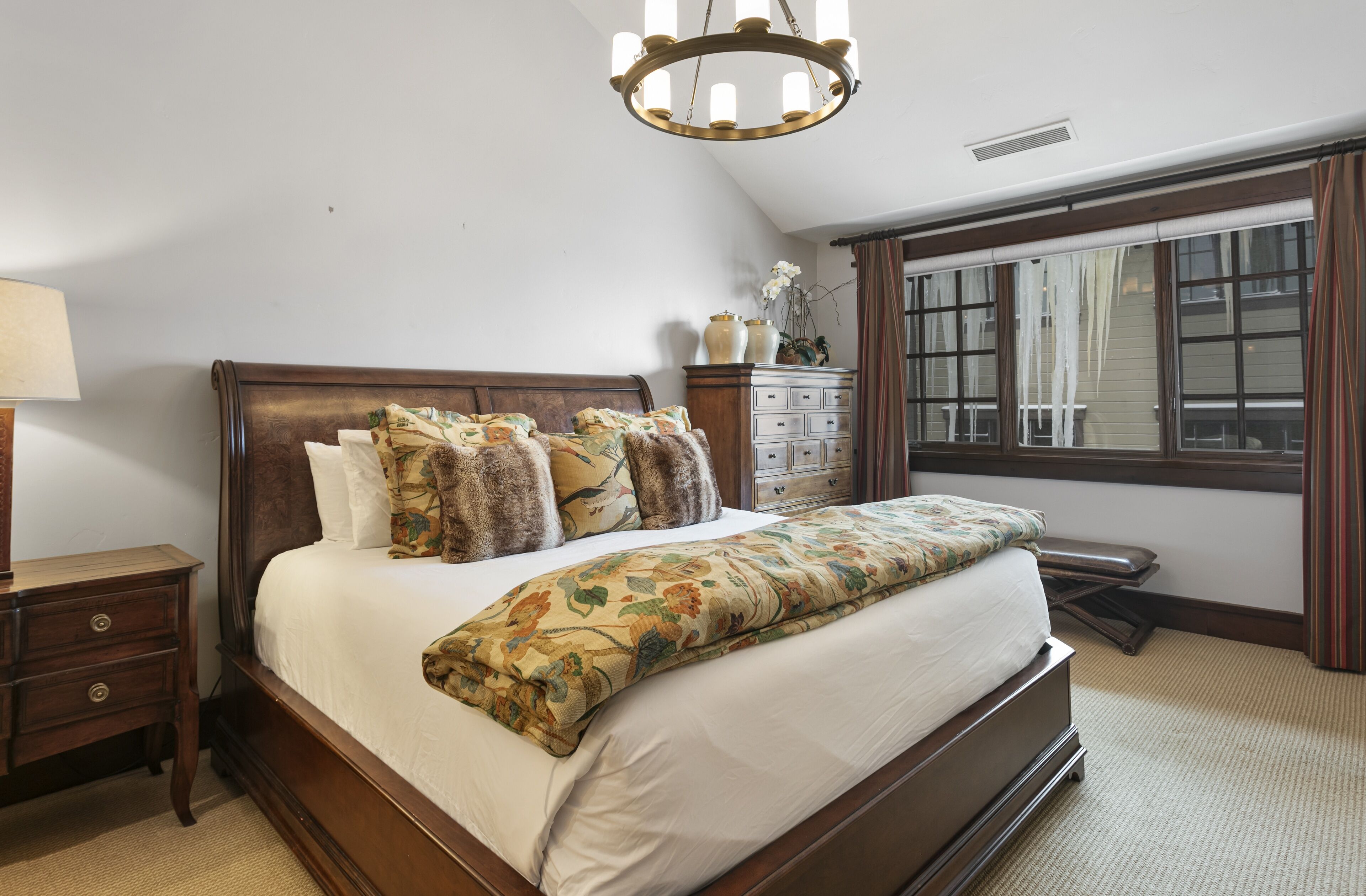 Un dormitorio con una cama de madera, una mesita de noche, un aparador y una ventana con cortinas.
