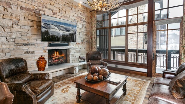 Una sala de estar acogedora con chimenea de piedra, mobiliario de cuero y un ventanal con vistas al exterior.
