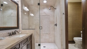 Un baño moderno con ducha envuelta en vidrio, un espejo grande y un lavamanos con encimera de mármol.