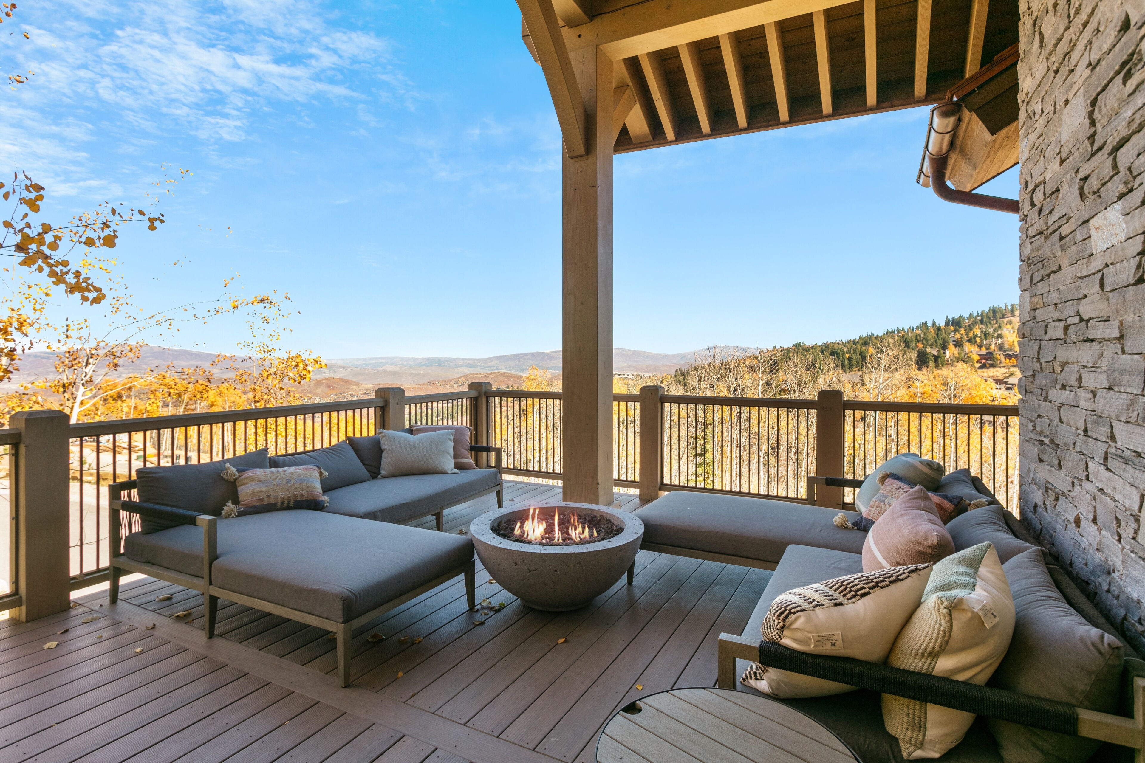 A covered outdoor seating area with a fire pit, cushioned sofas, and a view of the surrounding landscape.