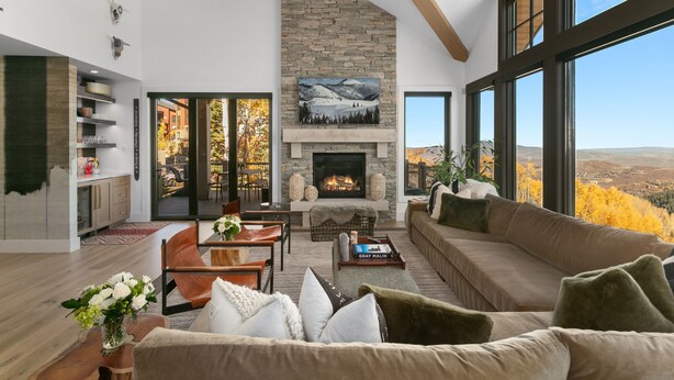 A spacious living room with a stone fireplace, a large window with a mountain view, and a cozy seating area. - Tower Villas - Five Bedroom Villa w/ Hot Tub #7700 by Deer Valley Resort (Park City)