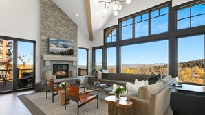 A spacious living room with a stone fireplace, large windows offering a mountain view, and a cozy seating area. - Tower Villas - Five Bedroom Villa w/ Hot Tub #7700 by Deer Valley Resort (Park City)