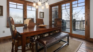 A dining room with a wooden table, leather chairs, and a bench. There are large windows with a view of the outdoors. - Grand Lodge - Three Bedroom Condo #201 - Ski-in/ski-out by Deer Valley Resort (Park City)