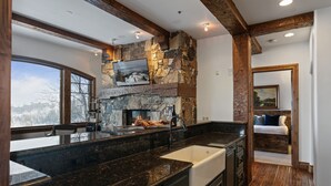 A kitchen with a stone fireplace, a large window, and a view of the mountains. - Grand Lodge - Three Bedroom Condo #201 - Ski-in/ski-out by Deer Valley Resort (Park City)