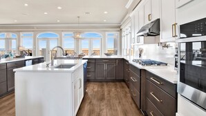 A spacious kitchen with a large island, modern appliances, and a view of the balcony. - Gulf and Lagoon Views | Elevator | Community Pool (Gulf Shores)