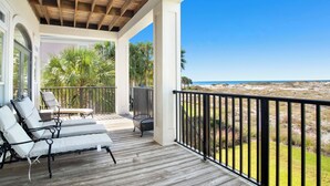 A wooden deck with lounge chairs and a table, overlooking a beach with palm trees. - Gulf and Lagoon Views | Elevator | Community Pool (Gulf Shores)