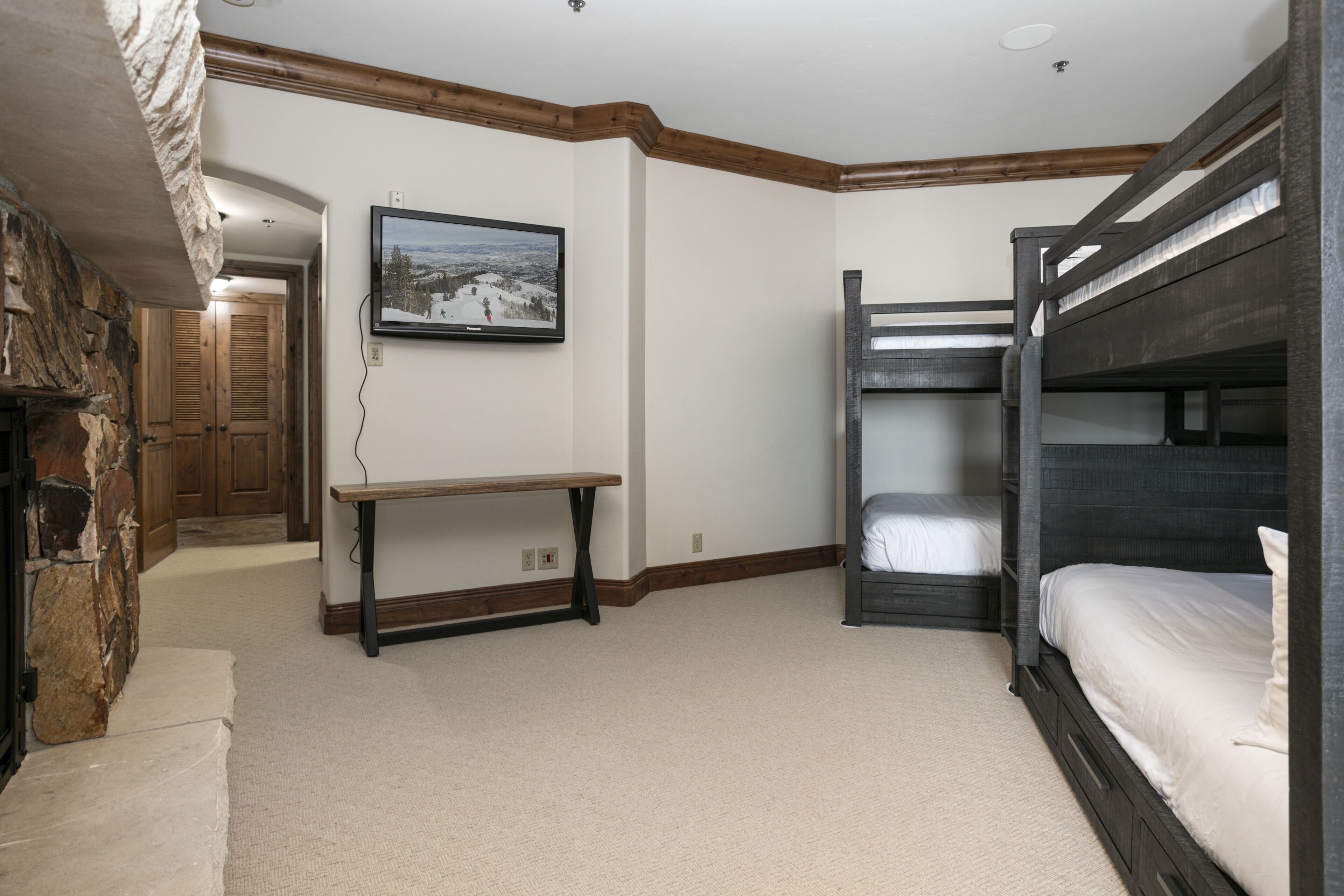 A room with bunk beds, a wooden bench, a stone wall, and a framed picture on the wall.