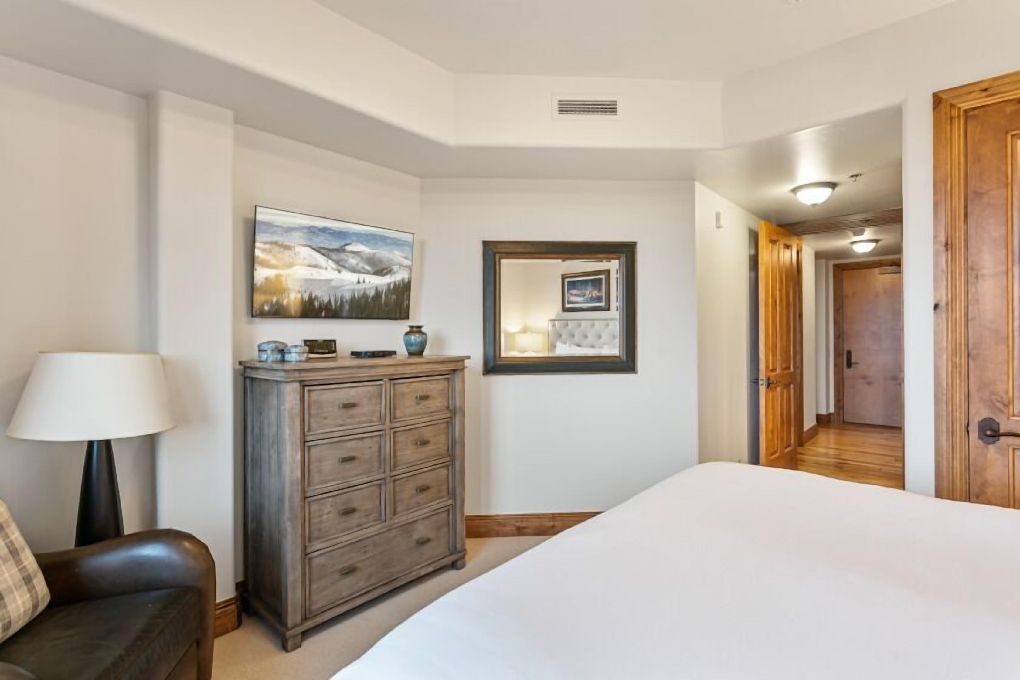 A bedroom with a bed, a dresser, a lamp, and a painting on the wall.
