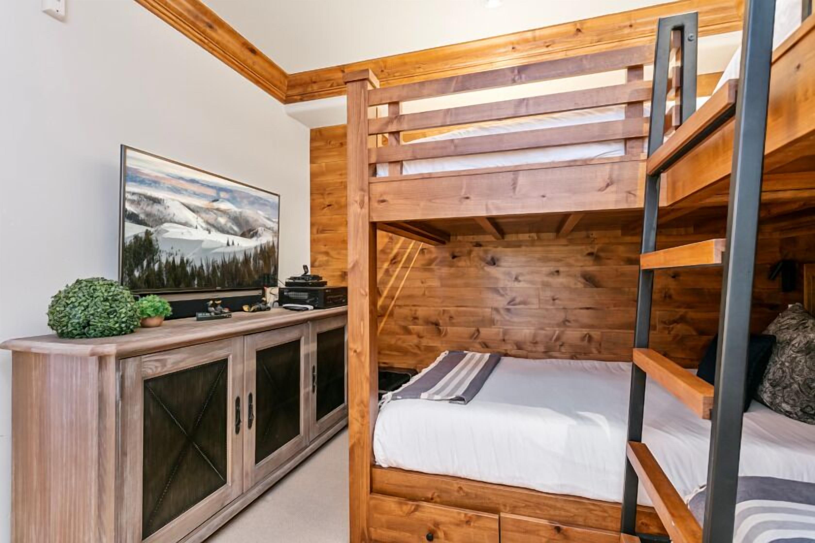 A bunk bed room with a wooden headboard, a television on the left, and a cabinet with glass doors.