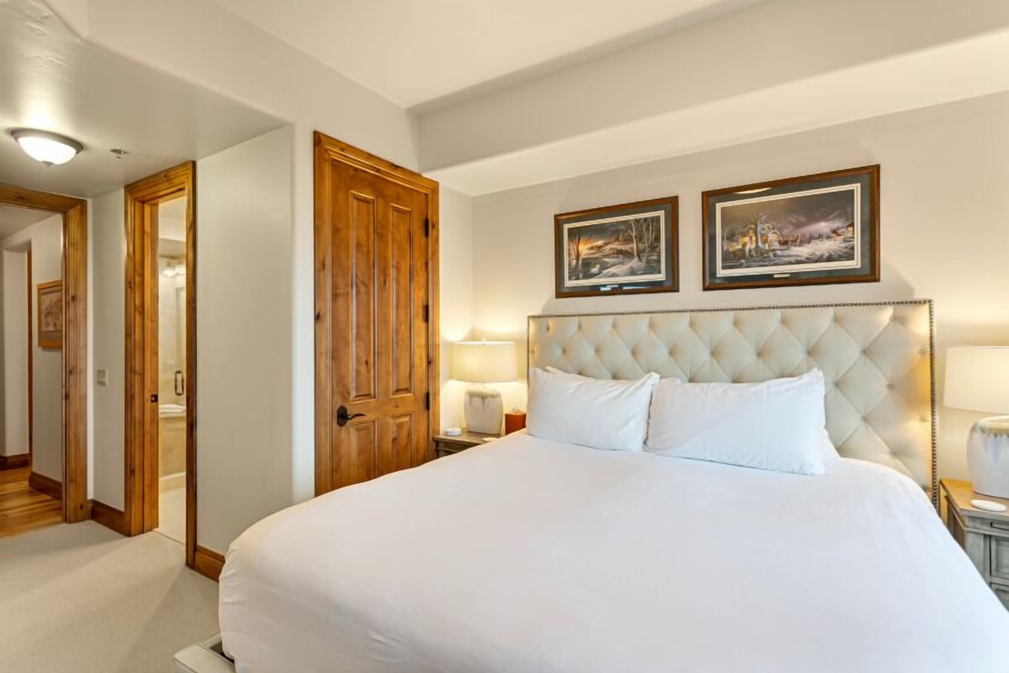 A hotel room with a large bed, wooden wardrobe, and two framed pictures on the wall.