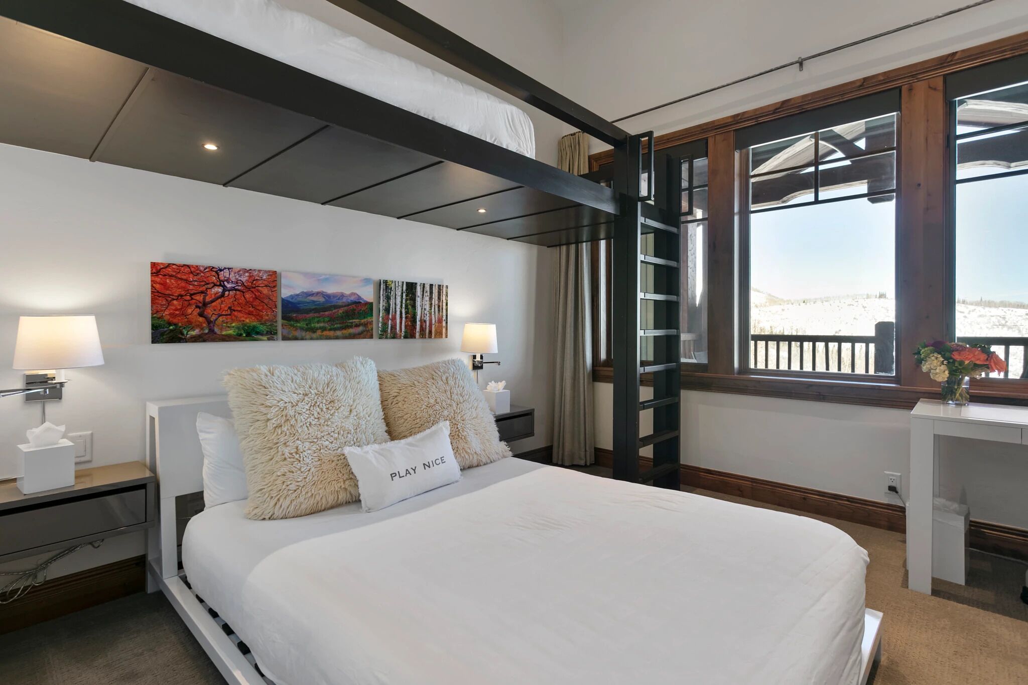 A bedroom with a bunk bed, a desk, and a large window with a view of a snowy landscape.
