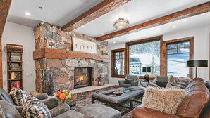 Un salon chaleureux avec une cheminée en pierre, des canapés en cuir et une grande fenêtre donnant sur un paysage enneigé.