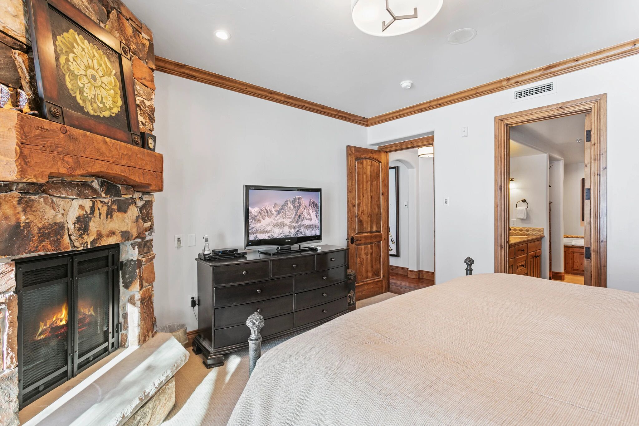A bedroom with a stone fireplace, a television, a dresser, and a large bed.