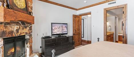 A bedroom with a stone fireplace, a television, a dresser, and a large bed.