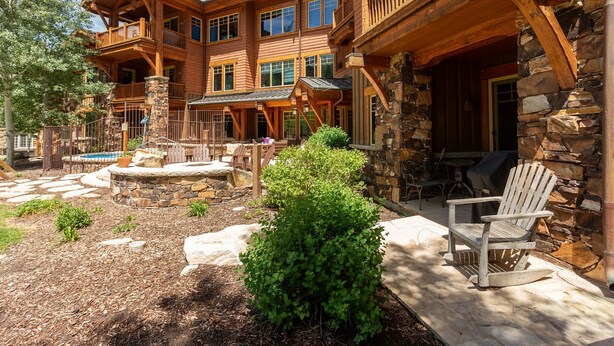 Une grande maison en bois avec une façade en pierre, un patio doté d’un foyer et des meubles pour s’asseoir à l’extérieur.