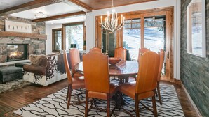 Un coin repas chaleureux avec une table en bois et des fauteuils en cuir, une cheminée en pierre et une vue sur un paysage enneigé par de grandes fenêtres.