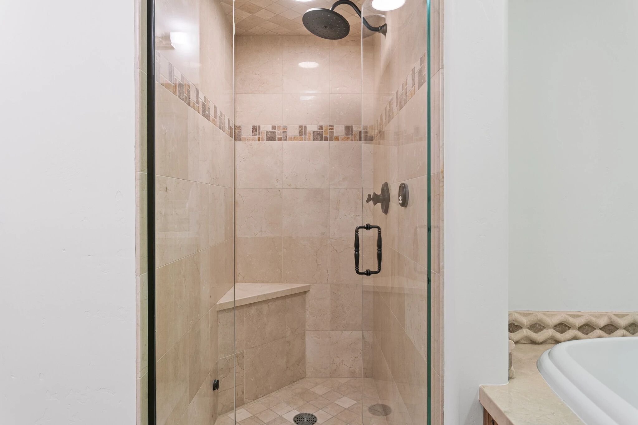A glass-enclosed shower with beige tiles, a glass door, and a showerhead.