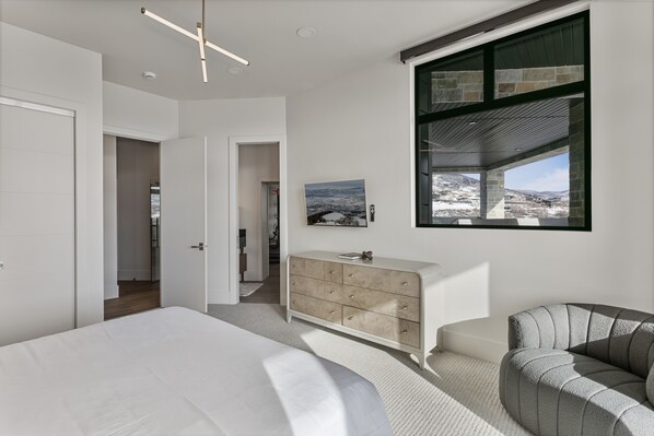Un dormitorio moderno con cama, cómoda y vista a un paisaje nevado a través de un ventanal grande.