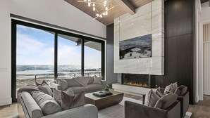 A modern living room with a large window, a fireplace, and a view of a snowy landscape.