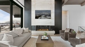 A modern living room with a fireplace, a sofa, a coffee table, and a view of a snowy landscape through a large window.