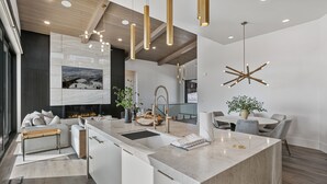 A modern kitchen with a central island, pendant lights, and a large window with a scenic view.