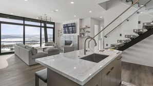 A modern kitchen with a large island, a built-in stove, and a view of a snowy landscape through large windows.