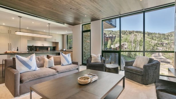 A modern living room with a large window, a sofa, a coffee table, and a view of a mountainous landscape.