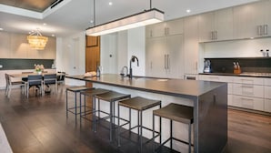 A modern kitchen with a central island, bar stools, and a chandelier.