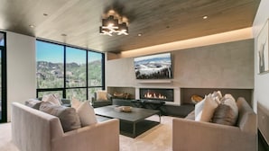 A modern living room with a fireplace, comfortable seating, and a large window offering a scenic view.
