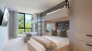 A modern bedroom with a bunk bed, a desk, and a large window offering a view of greenery.