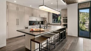 A modern kitchen with a central island, bar stools, and a large window offering a view of the outdoors.